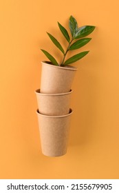 Vertical mockup image of kraft paper coffee cups with green leaves inside - biodegradable, compostable paper utensils for hot drinks. Paper cup on orange background with copy space. Selective focus