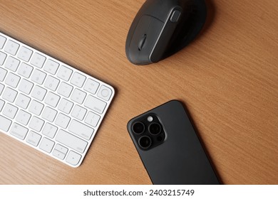 a vertical mouse, a keyboard and an iPhone lying on a wooden table. Apple Magic Keyboard Touch ID, 