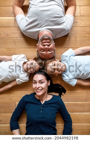 Vertical narrow shot portrait of happy young Caucasian family with small teen children lying on floor relaxing. Smiling parents with little teenage kids look at camera show unity love. Parenthood.