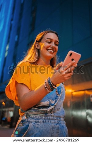 Vertical. one happy young girl using her smartphone to browse the internet while walking on the street at night. Female watching the social media with her cellphone. Girl typing on a mobile phone