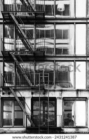 Vertical orientation black and white art photograph of classic vintage New York City loft building with fire escape and large glass window reflection.