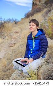 Vertical Orientation Color Image Of A Teenage Boy With Autism And Down's Syndrome With His Tablet Device Outside / Teenager With Autism And Down's Syndrome Outside With His Tablet Device