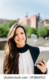 Vertical outdoors shot of a businesswoman standing in the street with tablet and looking at camera. - Shutterstock ID 593864912