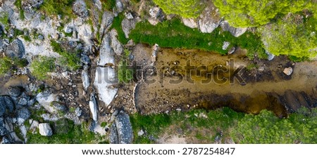 Vertical overhead drone angle displaying a narrow water channel flanked by green grass and imposing grey stones.