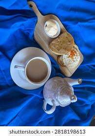 Vertical overhead flat lay of a cup of creamy coffee served beside an elegant floral ceramic teapot on vibrant royal blue fabric. Minimal beverage still life suitable for café, hospitality, and breakfast concepts with generous copy space.