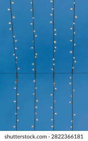 Vertical pattern of glowing Christmas lights against a blue twilight sky in Zaragoza, Spain. Festive holiday texture created by rows of hanging fairy lights in the Spanish city