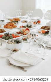 Vertical perspective looking down a long, elegantly served banquet table filled with glassware, white plates, and festive cold snacks.