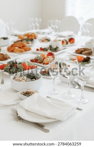 Vertical perspective looking down a long, elegantly served banquet table filled with glassware, white plates, and festive cold snacks.