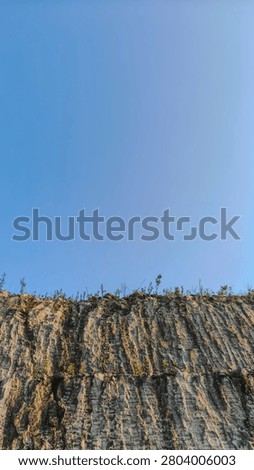 A vertical perspective looking up at a rocky retaining wall under a bright blue sky.