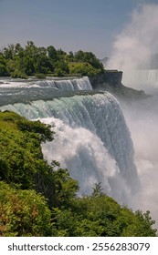 Vertical perspective view of Niagara Fall among green trees under blue sky on sunny day. View from American side. Beautiful nature landscape