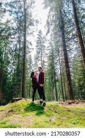 Vertical photo of a beautiful couple of hipsters in the woods, hugging and talking on a background of beautiful views. The couple is actively relaxing in the mountain forest