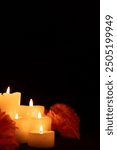 Vertical photo of burning candles nestled among marigolds on the left side, with a black background. The soft candlelight highlights the flowers, symbolizing Día de los Muertos traditions.