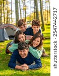 Vertical photo of a caucasian cheerful family laughing while lying down together at forest next to camping tent