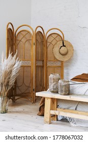Vertical photo of comfort apartment in bohemian style interior with hygge bedroom, hat on bamboo dressing screen, dry plants in vase, home decor in wicker basket