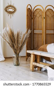 Vertical photo of cozy apartment in boho chic style interior with comfort bedroom, bamboo dressing screen near bed, home decor, dry plants in vase, mirror on white wall
