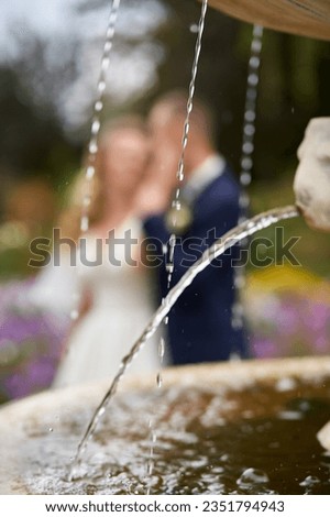 Vertical photo of drops of water flowing from a stone fountain and newlyweds in the background in defocus
