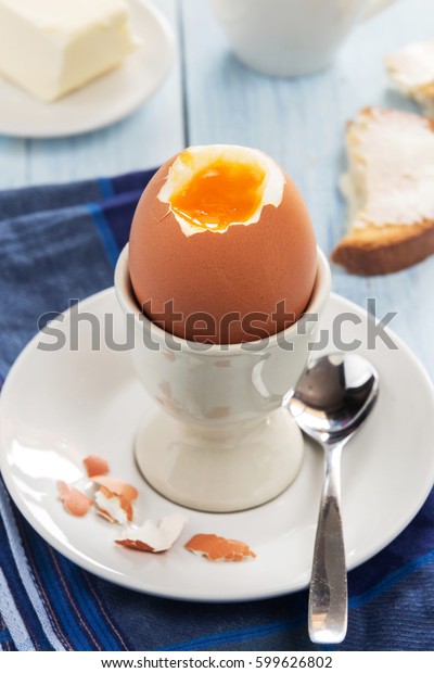A vertical photo of an egg in an egg-cup with\
toasts and butter