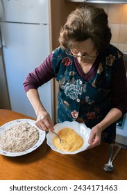 Vertical photo with elevated view of an aged woman beating eggs at home making handmade croquettes