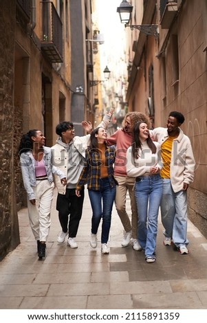 Vertical photo of a group of young happy friends walking in the street of the city. Smiling students laughing and having fun togethers
