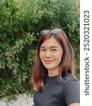 Vertical photo of happy asian Thai woman taking selfie while walking outdoor with green tea background on sunny day.