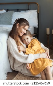 Vertical photo of happy young mother and daughter. Tender mom and baby girl sitting on floor and hugging at domestic living room with modern retro interior. Happy mothers day. 