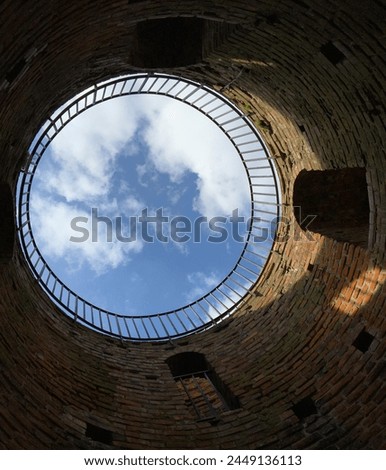 A vertical photo of the interior of an old round tower with a view of the sky .