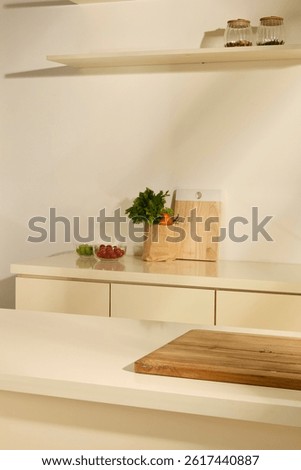 Vertical photo of the kitchen room. Vegetables in paper bags, next to glass bowls of tomatoes and green grapes. Empty wooden cutting board placed on white table in the middle of the kitchen