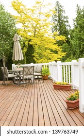 Vertical Photo Of A Large Outdoor Natural Cedar Deck With Patio Furniture And Bright Yellow And Green Trees In Background