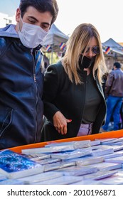 Vertical Photo Latino Hispanic Man Wearing Medical Masks With His Partner A Latina Woman At A City Fair, Looking Through Books