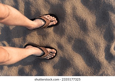 Vertical photo of a male feet in flip flops standing at the sand beach in summer at the sunset - Powered by Shutterstock