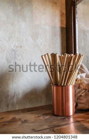 Vertical photo of natural color bamboo straws in rose gold bronze cup  on wooden table with loft concrete background
