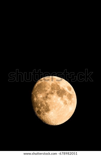 Vertical photo of nice golden moon with visible\
craters on the edge of shadow. The moon is almost full with just\
small part hidden in the dark. The light and dark parts on surface\
are clearly visible.