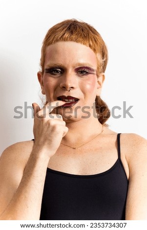 Vertical photo of a non-binary redhead is posing on a white background while biting a nail looking at camera. Concept of non-binary people, is not identified with any gender. Support for LGBTI.