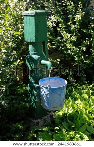 A vertical photo of a old water pump with a pail handing off of it