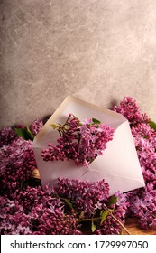 Vertical photo of purple flowers in an envelope. Bunches of lilacs surrounding letter. Copy space in upper part of image. Envelope slightly tilted.