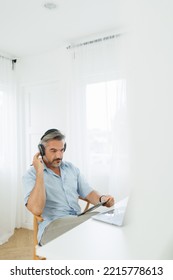 Vertical Photo Of Serious Senior Mature Adult Man In Headphones Using Digital Tablet And Laptop Computer, Online Meeting, Working At Home. Video Call, Video Conference.