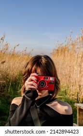 Vertical Photo of a Short-haired Girl Taking a Picture with a Red Retro Compact Camera in a Rice field with Tall Plants Background - Shutterstock ID 2142894423