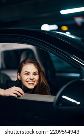 Vertical Photo From The Side, At Night, Of A Woman Sitting In A Car And Looking Out Of The Window, Laughing Happily Into The Camera, Closing Her Eyes