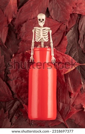 vertical photo of a skeleton peeking out of a red vase against a background of red tree leaves. autumn longing