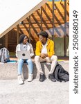 Vertical photo of two african students using laptop sitting outside the university building