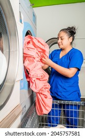 Vertical Photo Of A Woman Standing In Front Of A Washing Machine Picking Up A Sheet In A Laundry