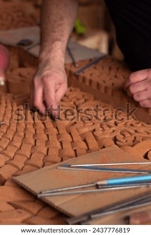 Vertical photo. Yerevan, Armenia. Male hand closeup. Adult man restores medieval Armenian khachkar called khachkar. Сraftsman polishes religious red brick slab with pattern. Work tools. Old grave. Job