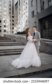 Vertical Photo Of Young Couple Just Married On City Background. Professional Wedding Photoshoot Stand Stairs City Outside