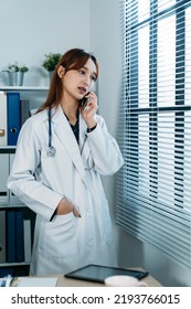 Vertical Photograph Japanese Woman Physician Putting Hand In Pocket And Looking Outside The Window While Having A Phone Discussion In The Office With Daylight.