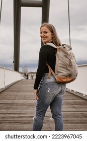 Vertical photography of a young woman with a huge bag on her back; the woman is standing in the middle of a bridge looking backwards - Shutterstock ID 2223967045