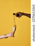 Vertical pop color concept of hands pouring champagne in glass on vibrant yellow background