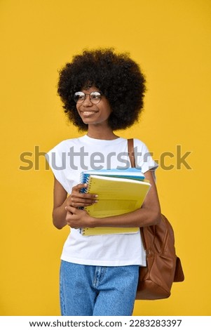 A vertical portrait of african american girl with curly afro hairstyle stands with backpack and holds exercise books on a yellow background. Smart student looking aside on orange wall with copy space.