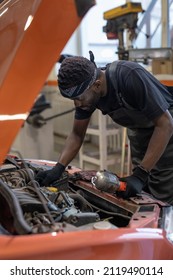 Vertical portrait of African-American male mechanic looking under hood while repairing car in auto shop