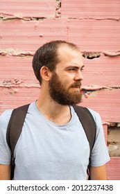 Vertical Portrait Of Bearded Confident Serious Spanish Man Wearing Backpack Looking To The Right On A Pink Bricks Background. Urban People Concept With Copy Space