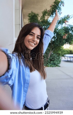 Vertical portrait of beautiful Caucasian woman student taking selfie looking at camera with toothy smile while stands outside University campus after classes.
